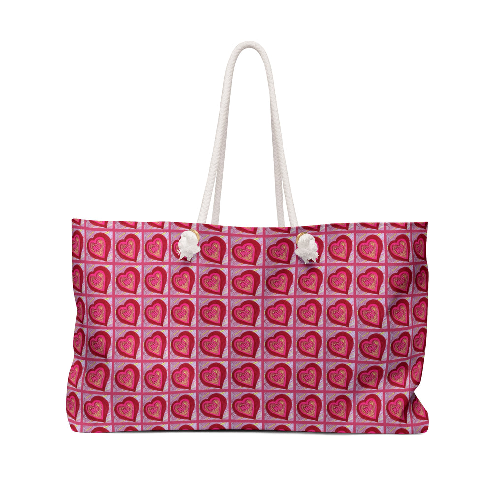 Oversized pink and red weekender tote bag with a repeating heart pattern and thick cream rope handles.
