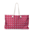 Oversized pink and red weekender tote bag with a repeating heart pattern and thick cream rope handles.