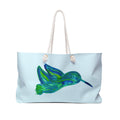 Large sky-blue weekender tote bag featuring a beautiful watercolor pattern of emerald and teal hummingbirds with thick cream rope handles.