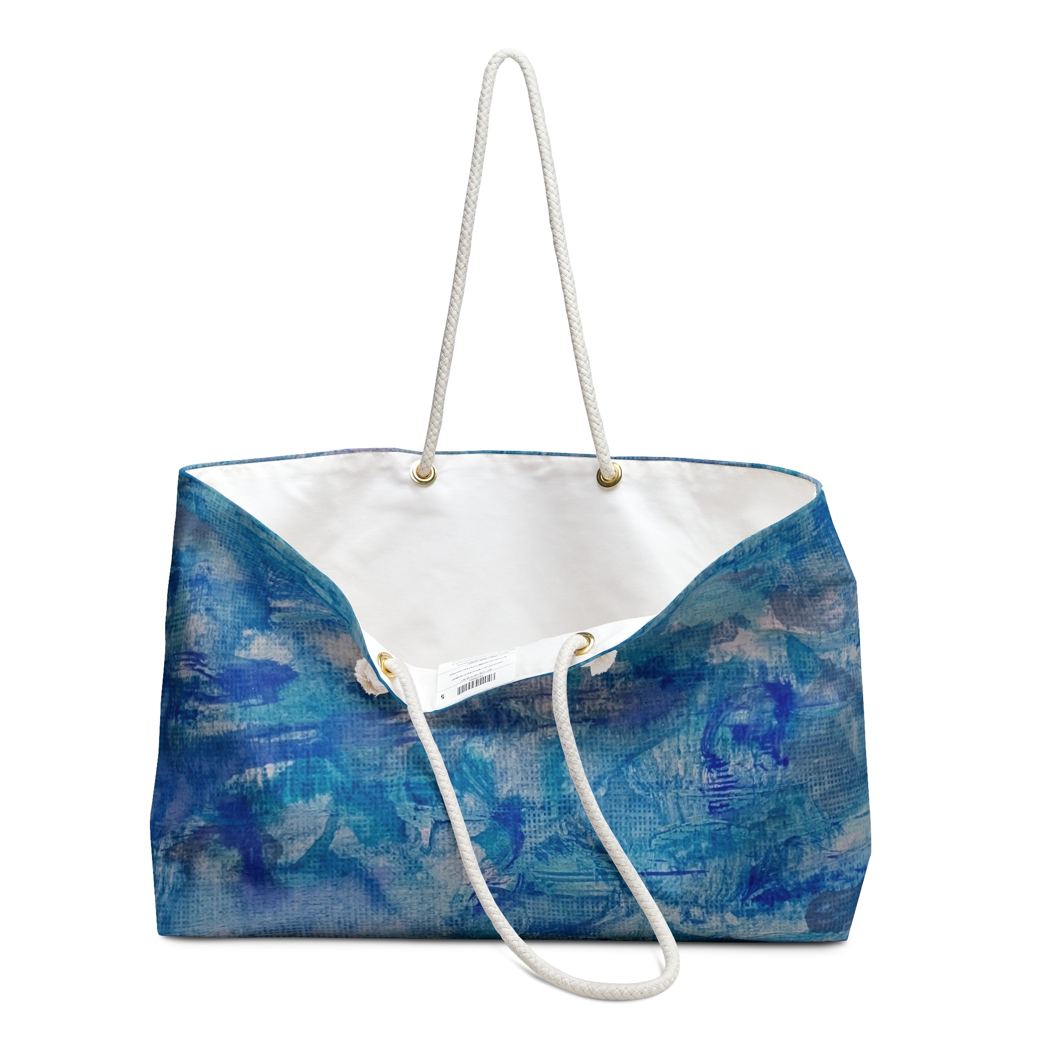 A canvas tote bag featuring an abstract blue and white painted pattern on the exterior, a white interior lining, and thick white rope handles with gold-tone metal hardware. Watercolor beach bag of ocean waters.